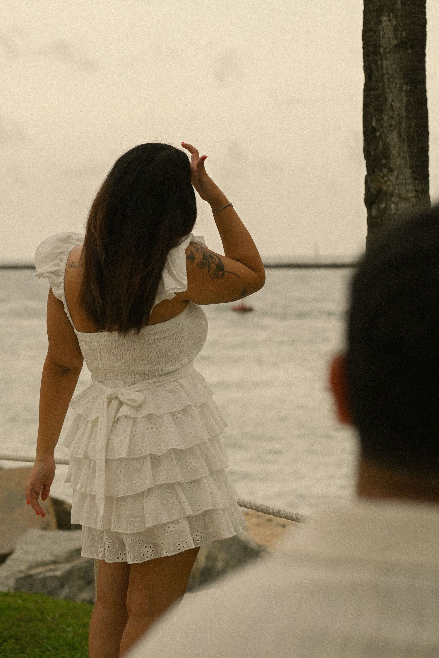 A woman in a white ruffled dress dances by the waterfront during sunset.
