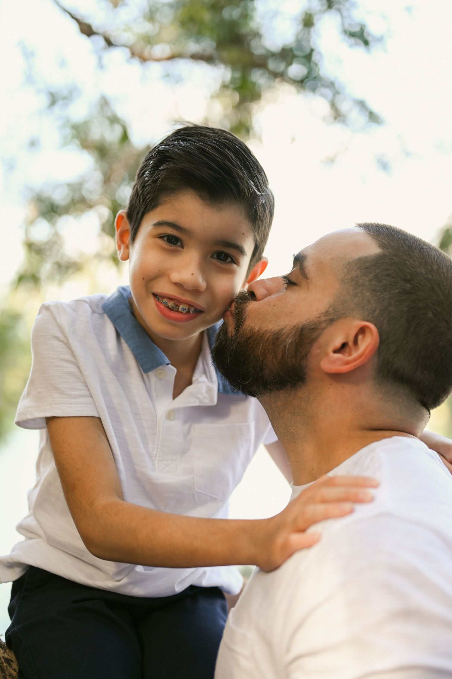 Father and son sharing affectionate moments outdoors in natural lighting.