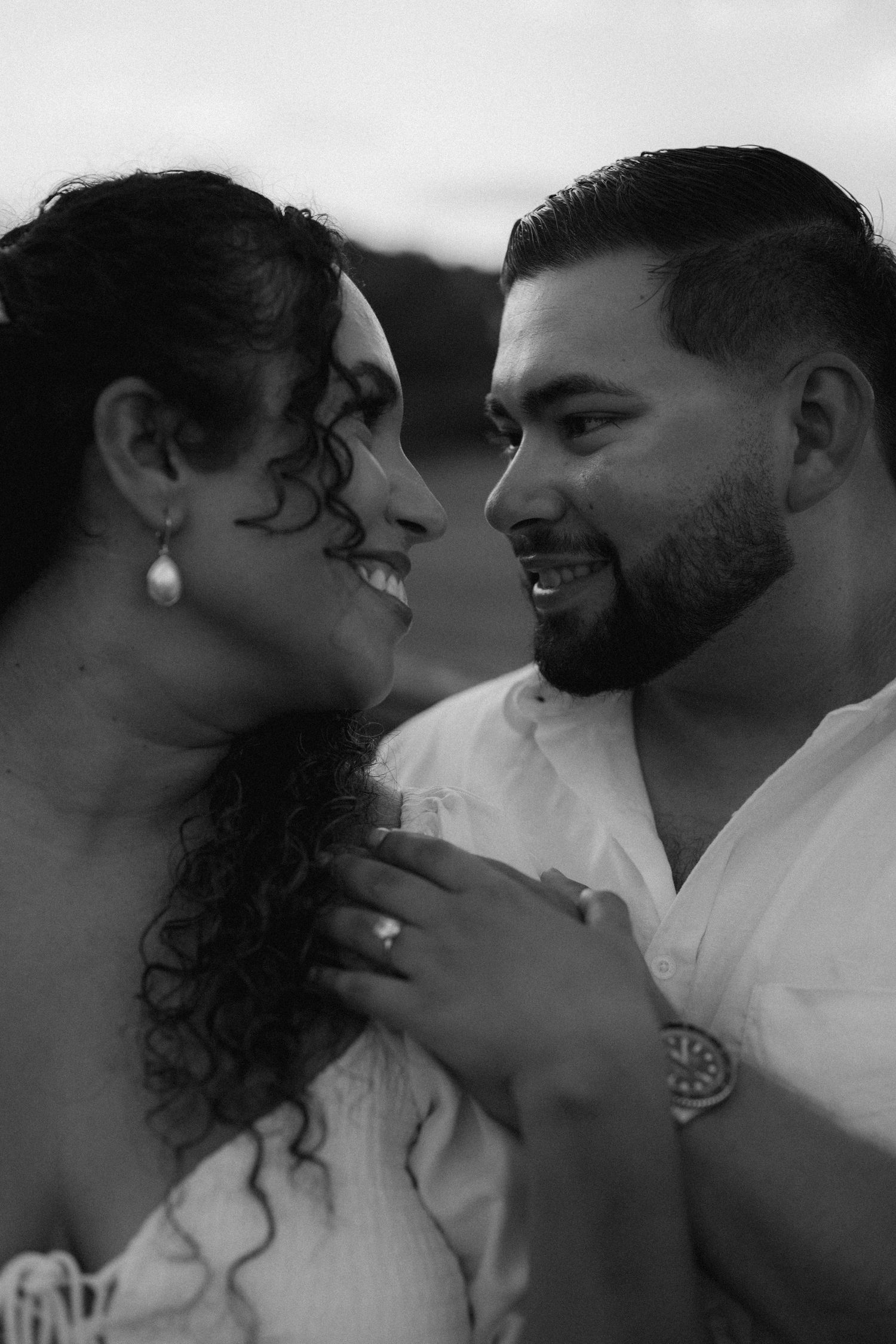 Black and white photo of a smiling couple in an intimate moment, woman with curly hair and man in white shirt embracing closely.