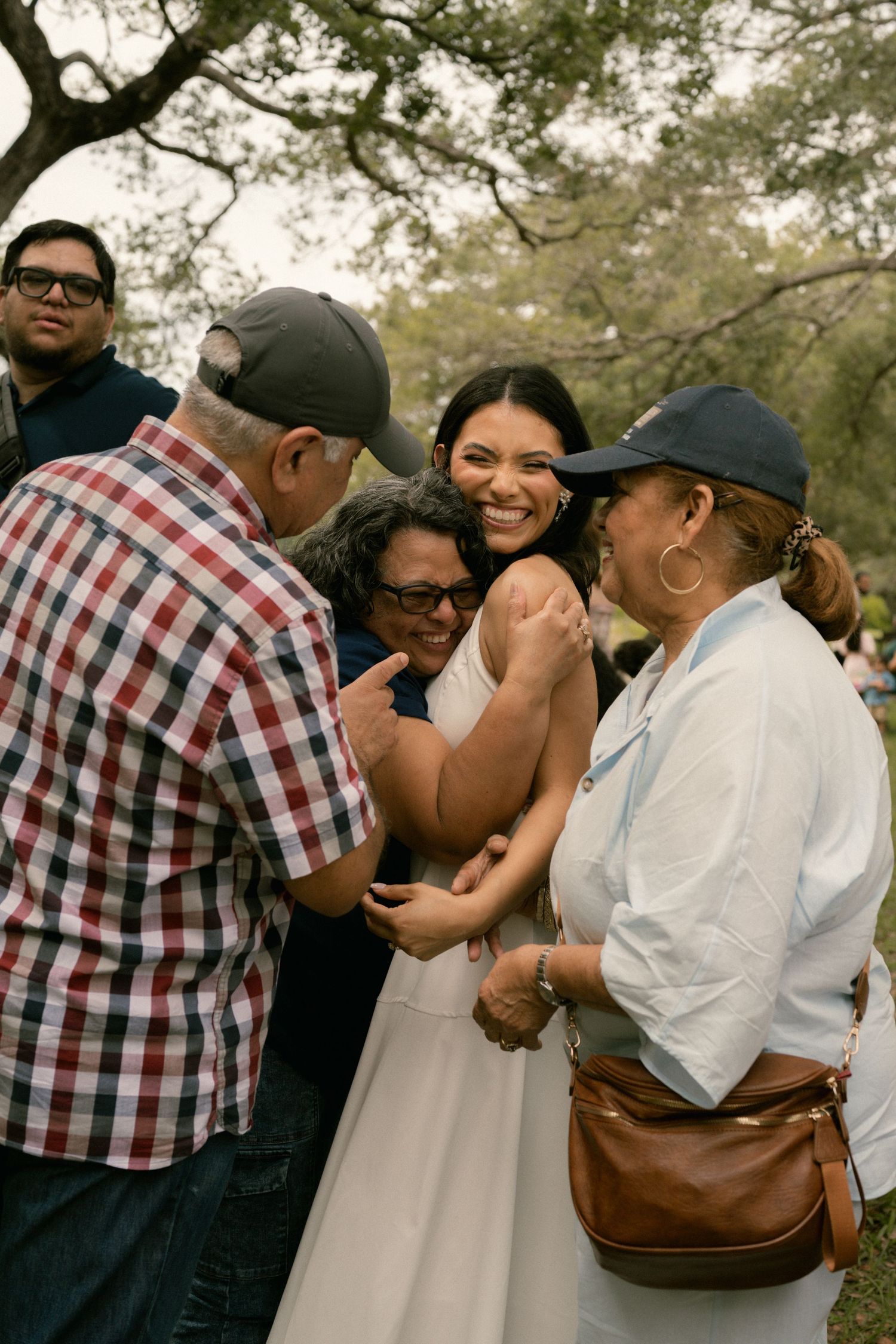 Bride in white dress joyfully greeted by family members at an outdoor wedding reception.