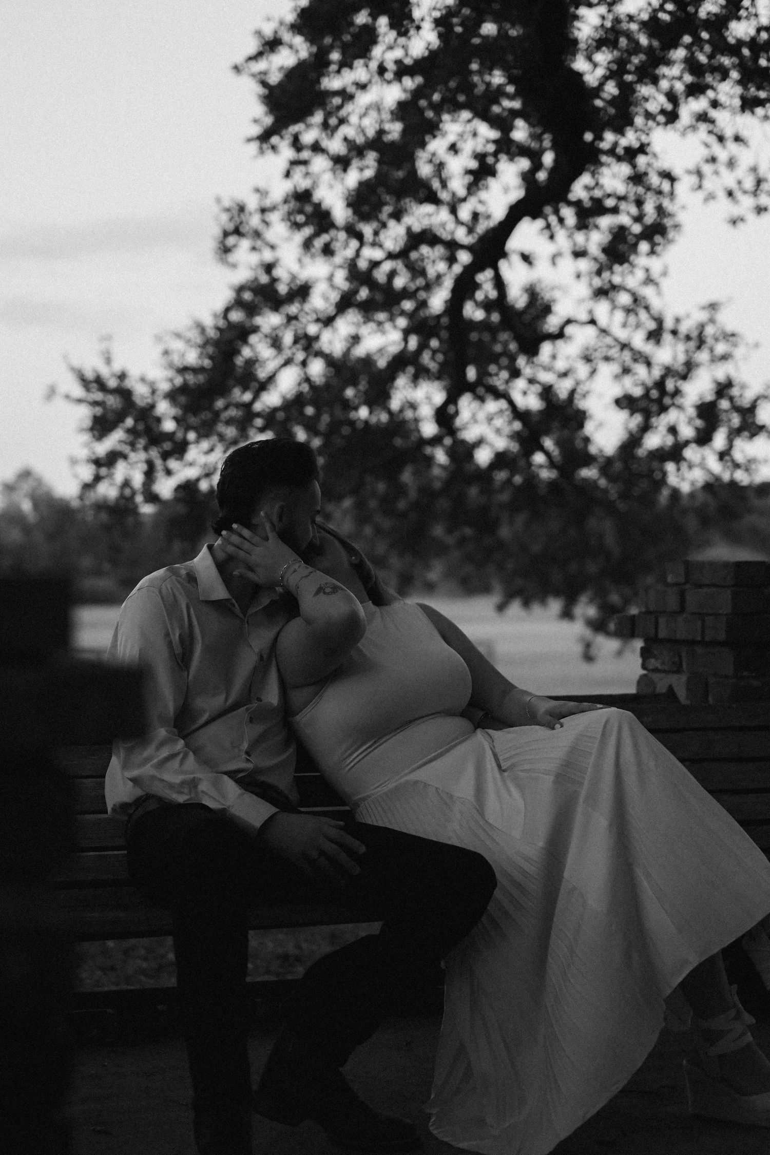 A couple reclines on a bench in a romantic pose during sunset.