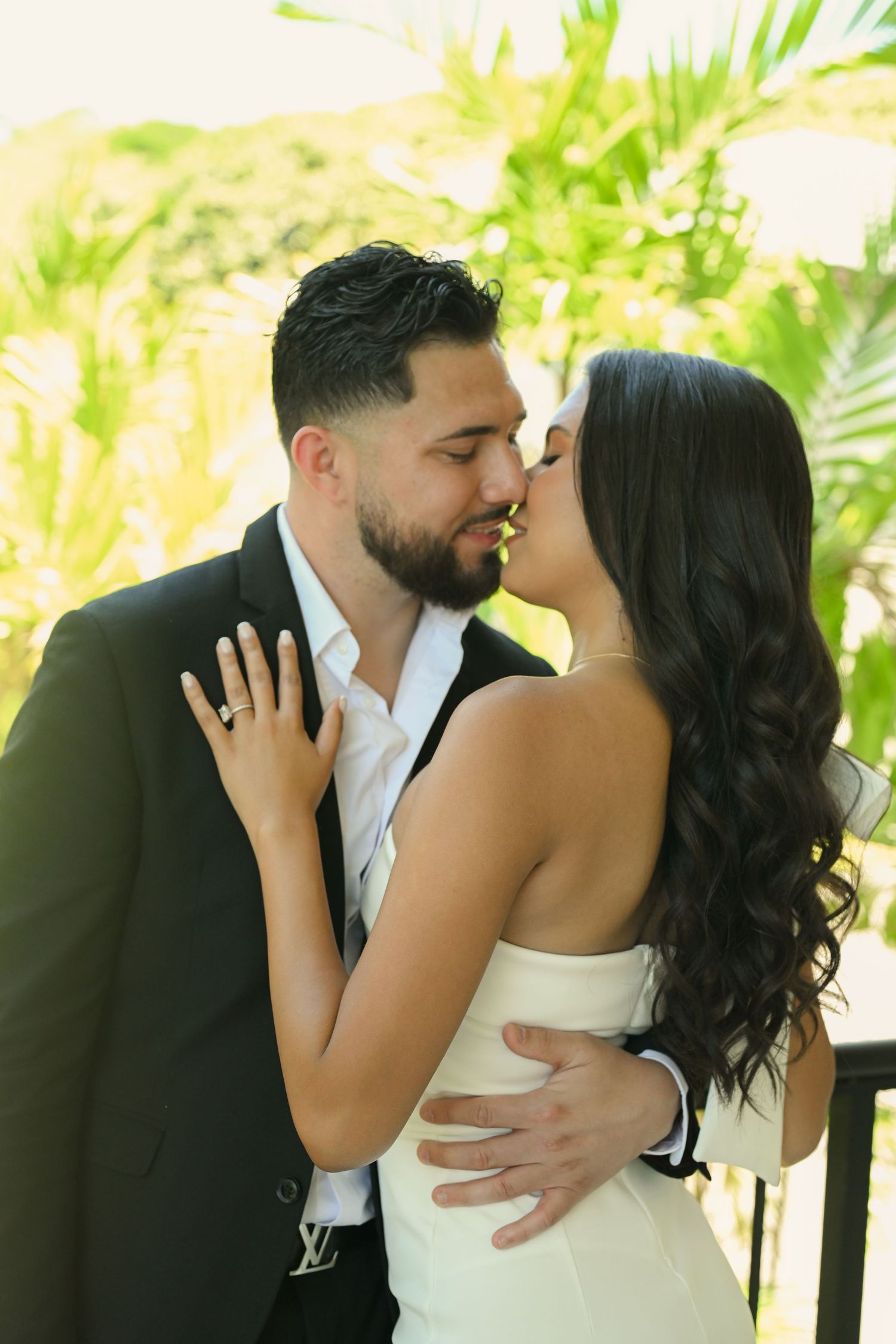 A romantic couple shares an intimate moment in a garden setting, dressed in formal attire.
