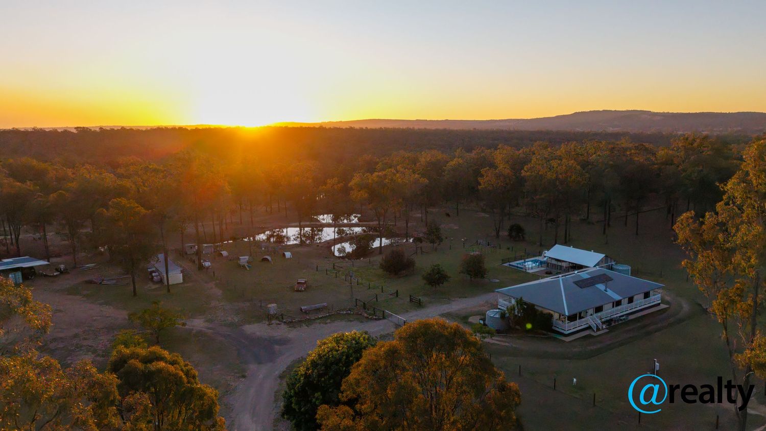 Aerial sunset view of a rural Australian property with a dam, caravans, and eucalyptus trees glowing in golden light.