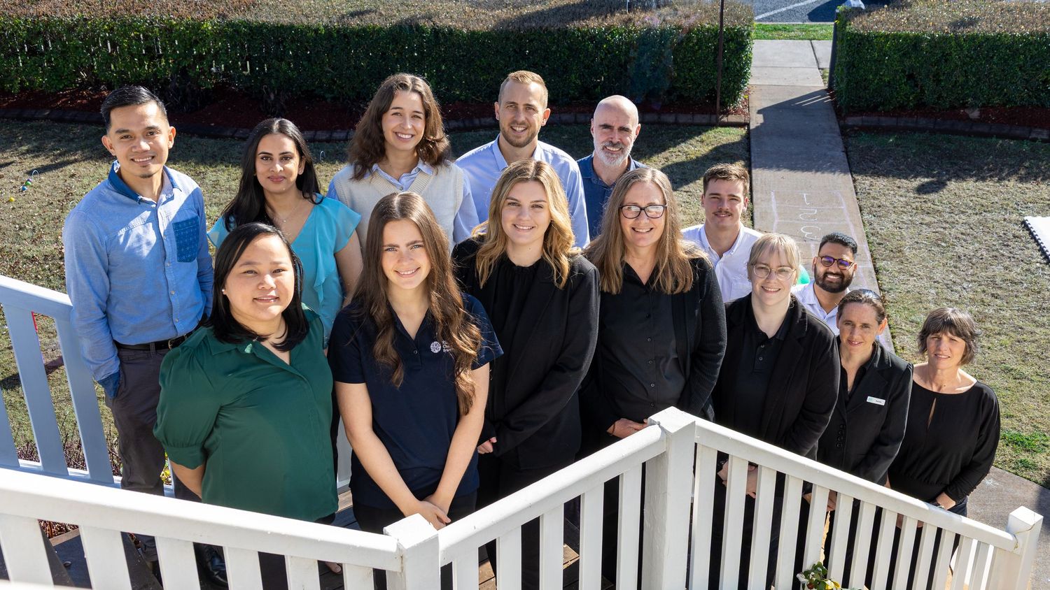 A professional team of diverse staff members posing together outdoors on white steps near a manicured lawn.