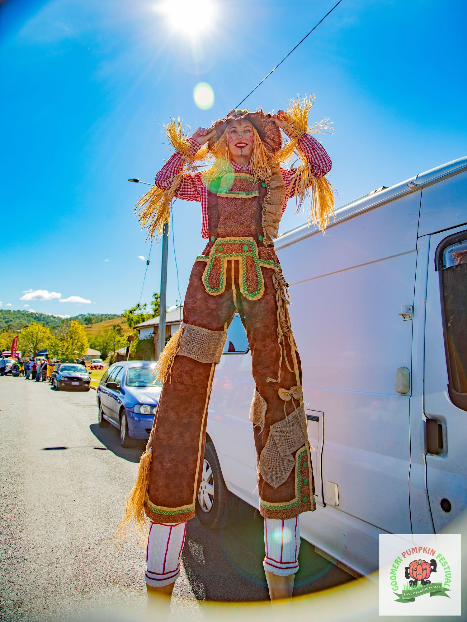 Performer on stilts dressed as a giant scarecrow costume posing outdoors on a sunny day.