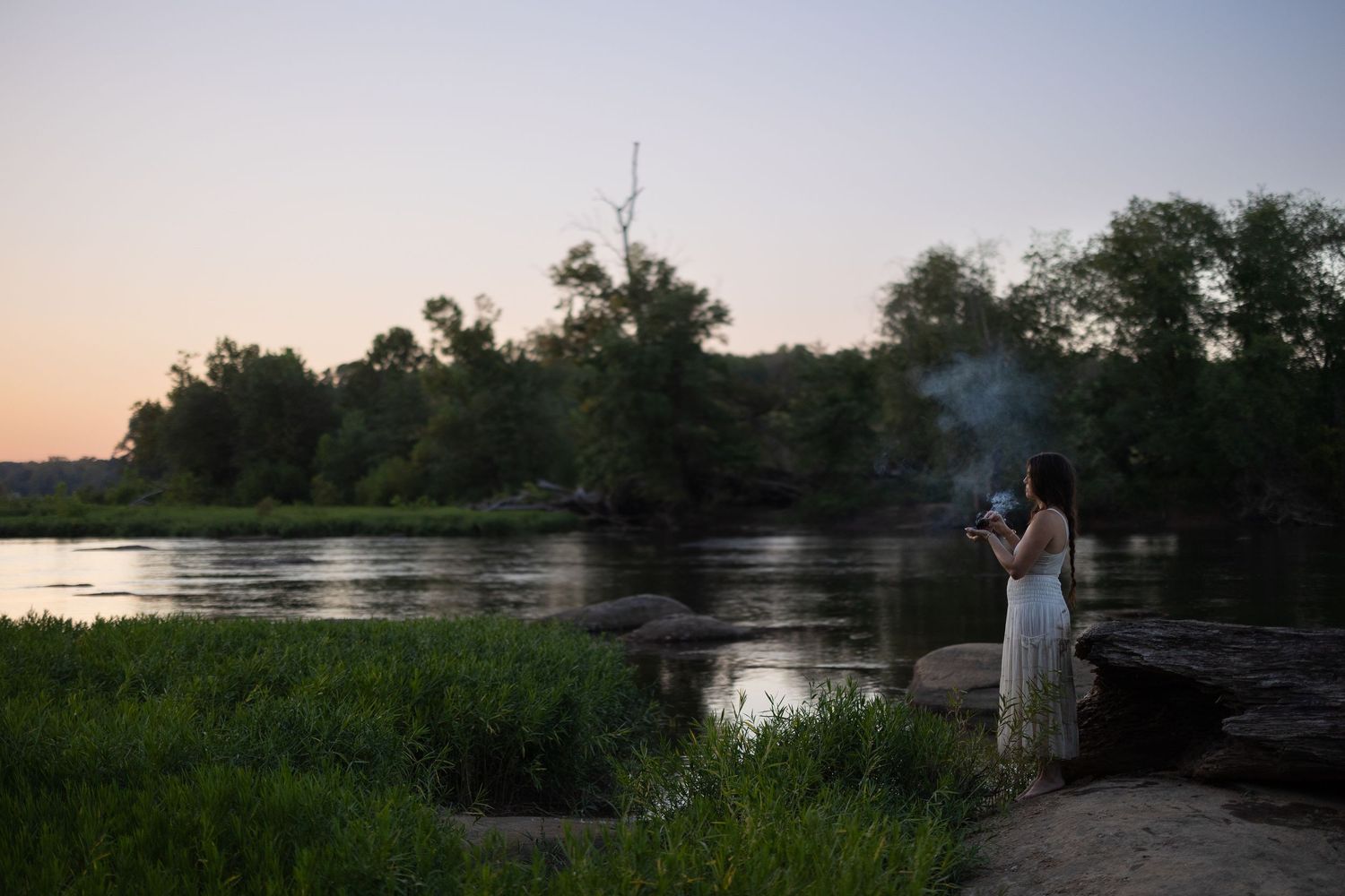 A serene river landscape with trees silhouetted against a tranquil sunset sky.