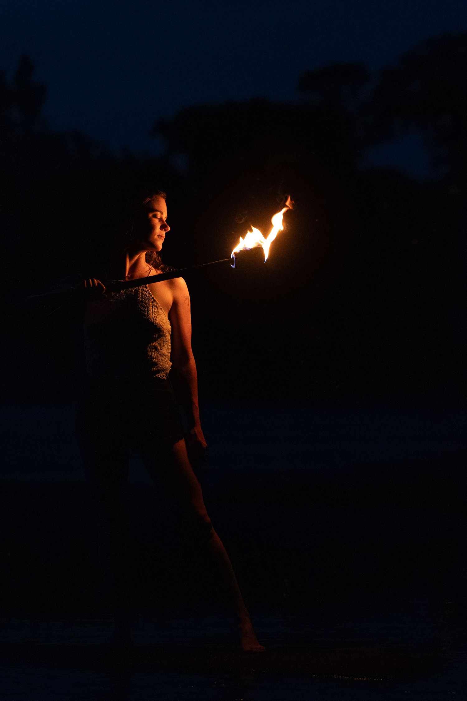 A dramatic nighttime scene with a fire performer holding a lit torch against a dark background.