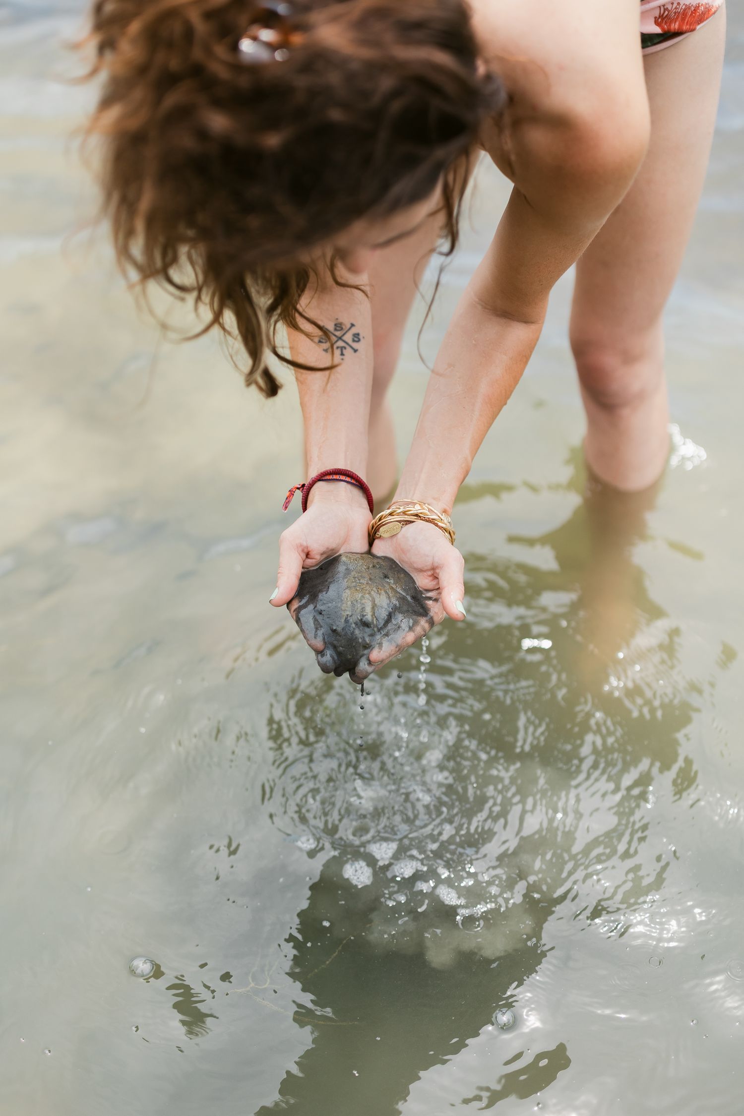 Person splashing water in a lake as they bend down to touch the surface with their hands.