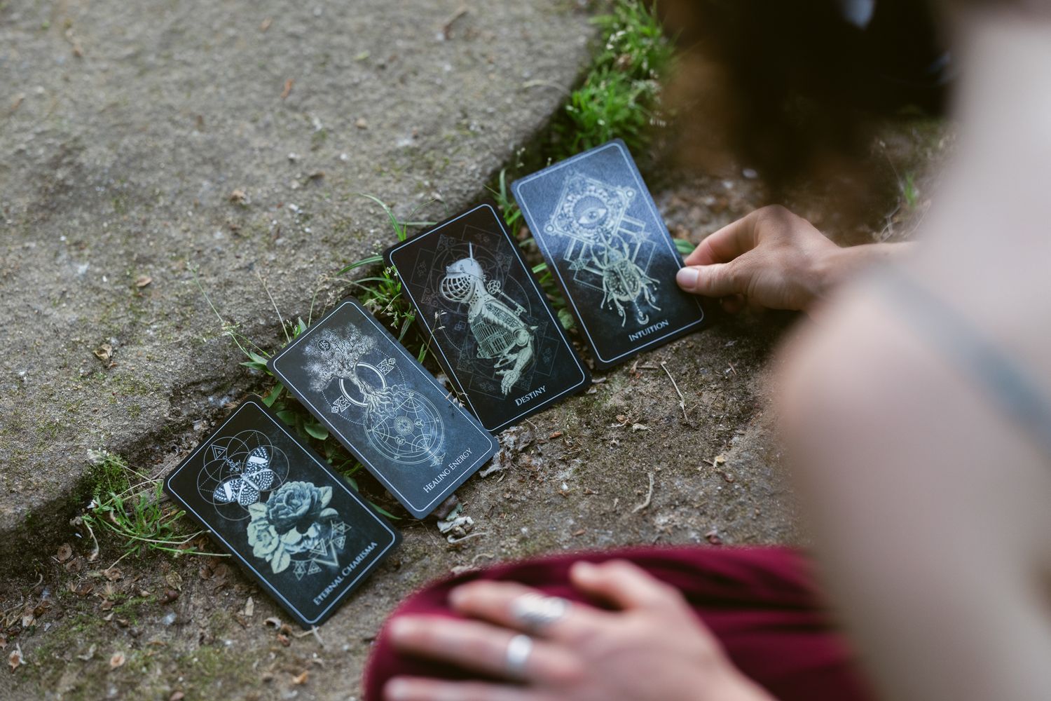Person looking at mystical tarot cards laid out on stone surface with moss in a dark moody setting.