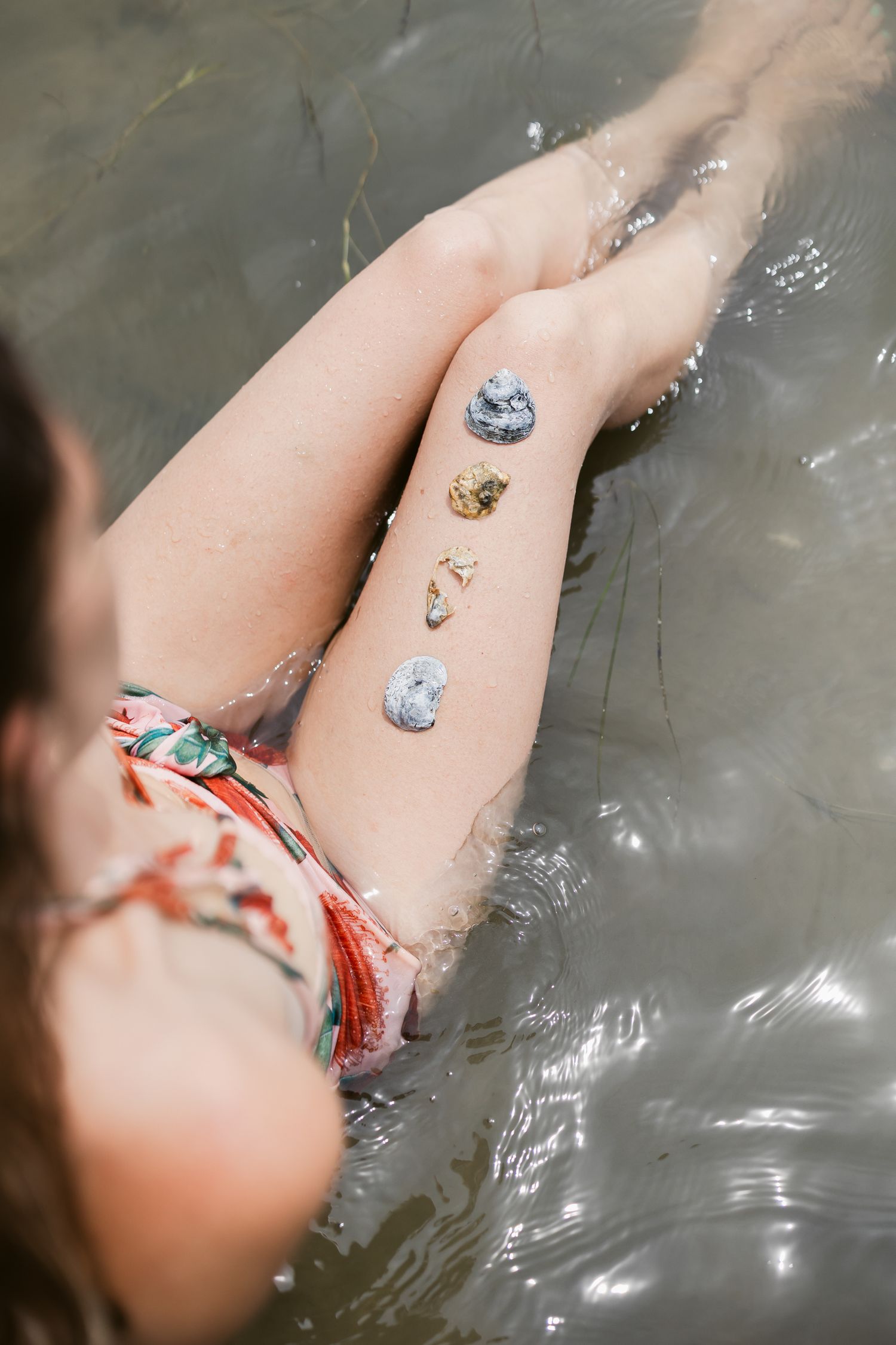 Leg with decorative glitter resting in dark water while wearing a floral print swimsuit or garment.