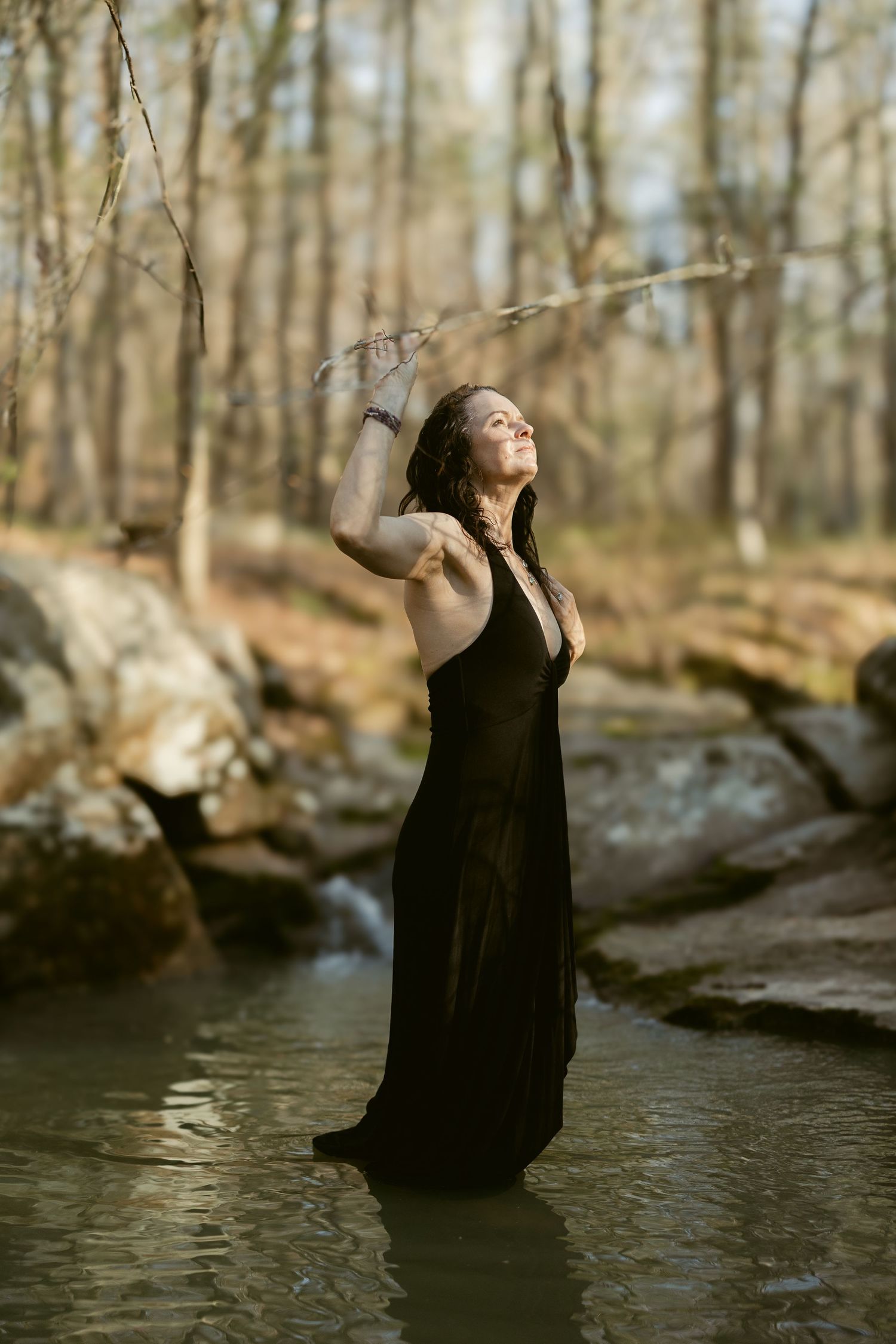 Evocative portrait series of a figure in a black dress standing in shallow water amidst a sunlit forest.