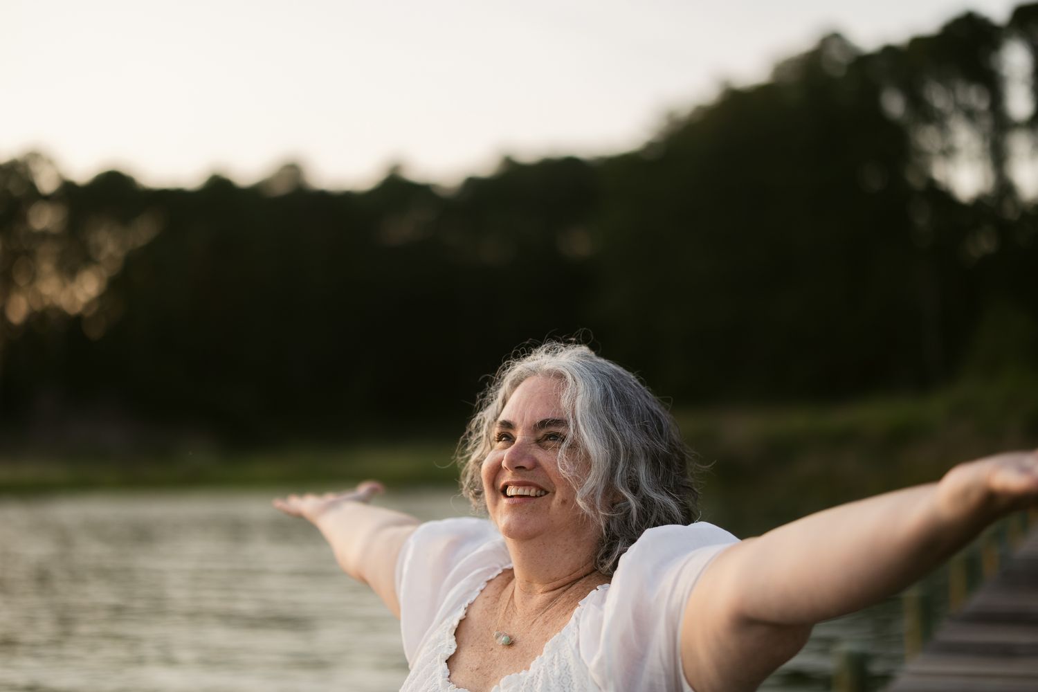 Joyful senior woman with gray hair spreading her arms wide while enjoying the sunset outdoors.