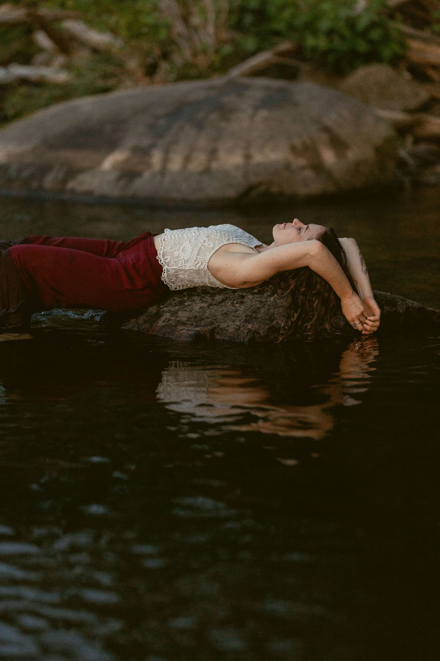 A person in white lace floats serenely on dark water in an artistic portrait session.