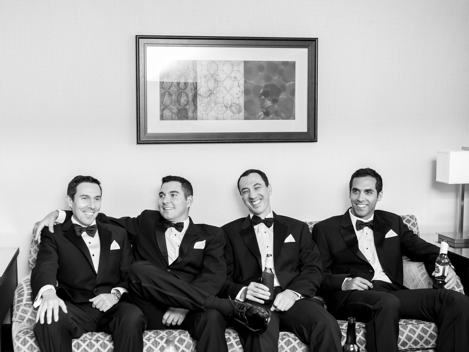 A black and white photograph shows a group of men in dark suits sitting together on what appears to be a couch.