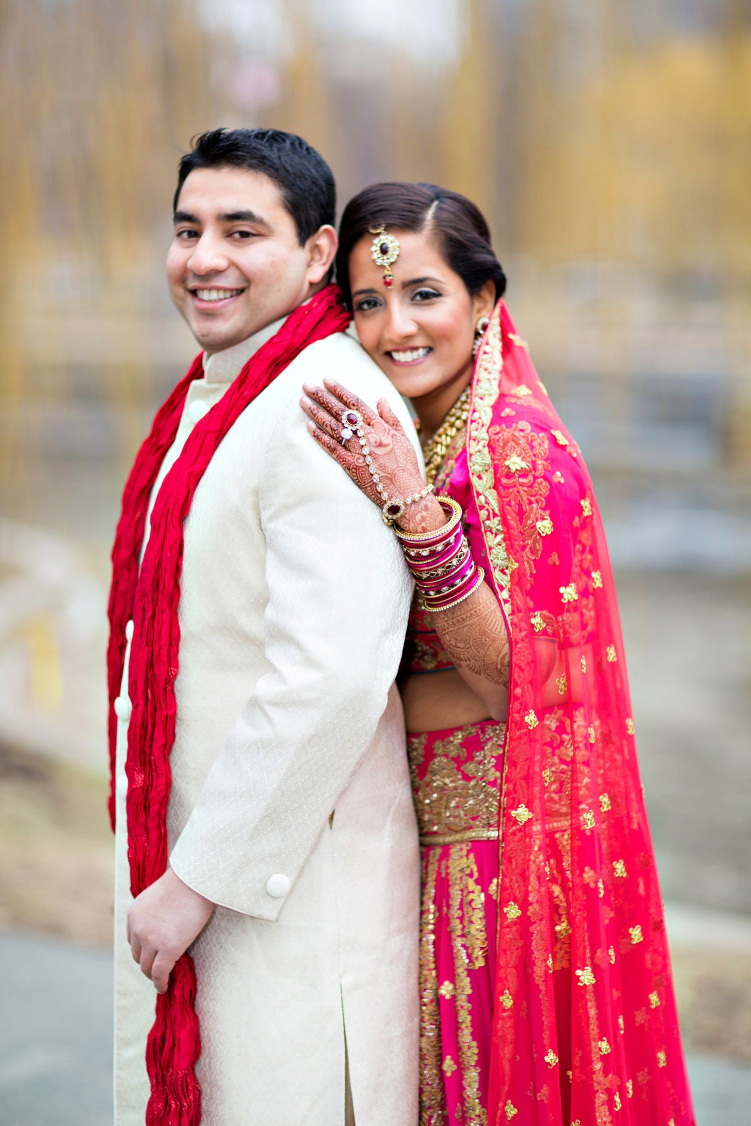 A couple in traditional South Asian wedding attire embraces and smiles in a romantic outdoor photo sequence.