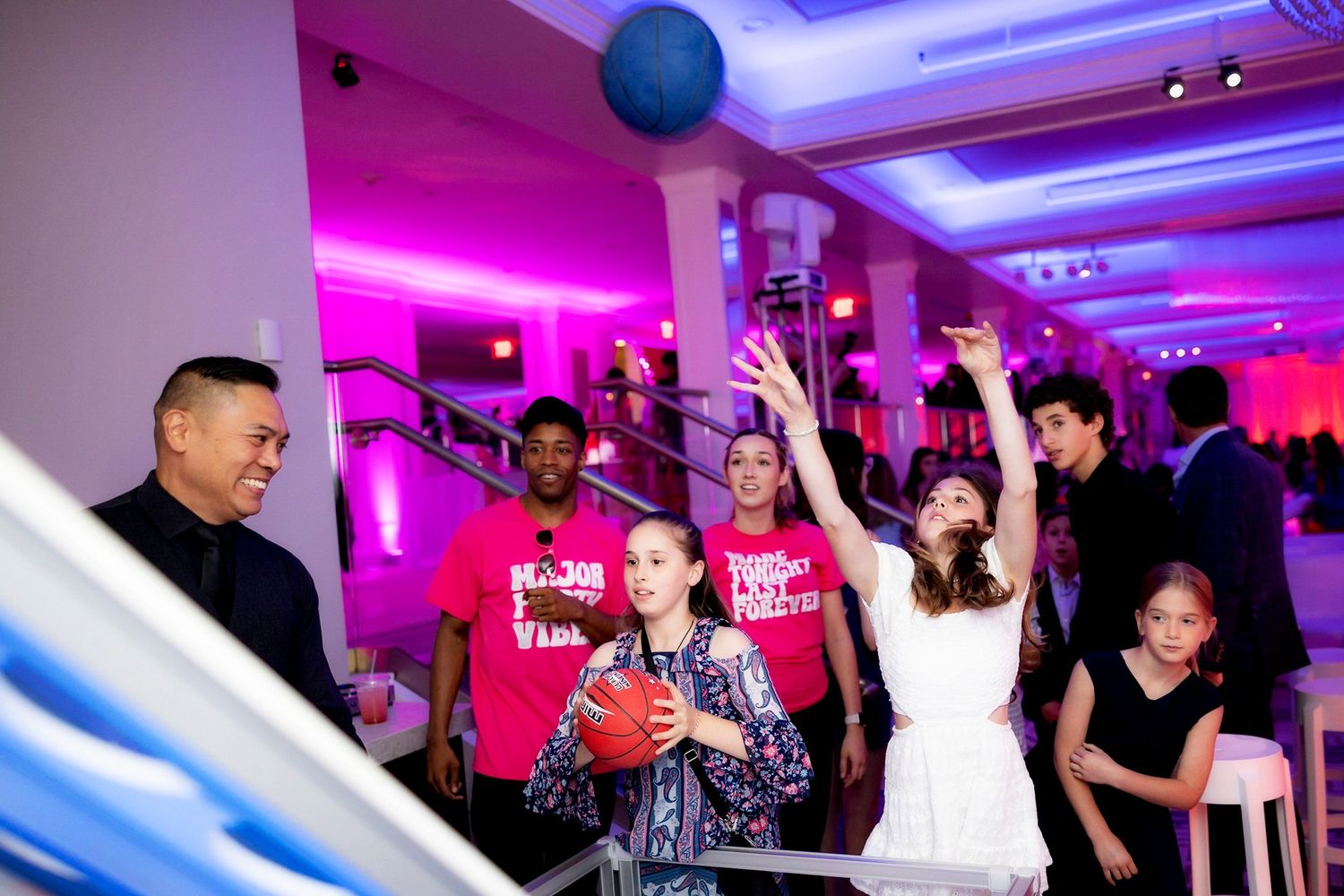 Energetic party crowd celebrating with hands raised under purple lighting at an event venue.