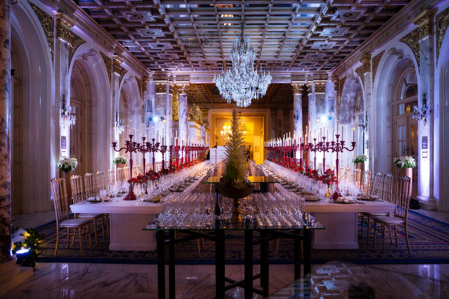 Elegant ballroom setup with crystal chandelier and long banquet tables arranged in rows for a formal event.
