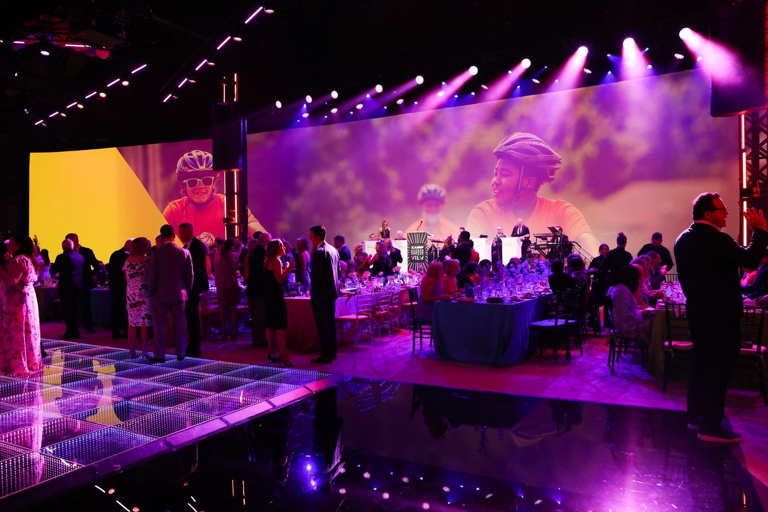 Crowded event space with purple lighting and LED dance floor creating an atmospheric party ambiance.