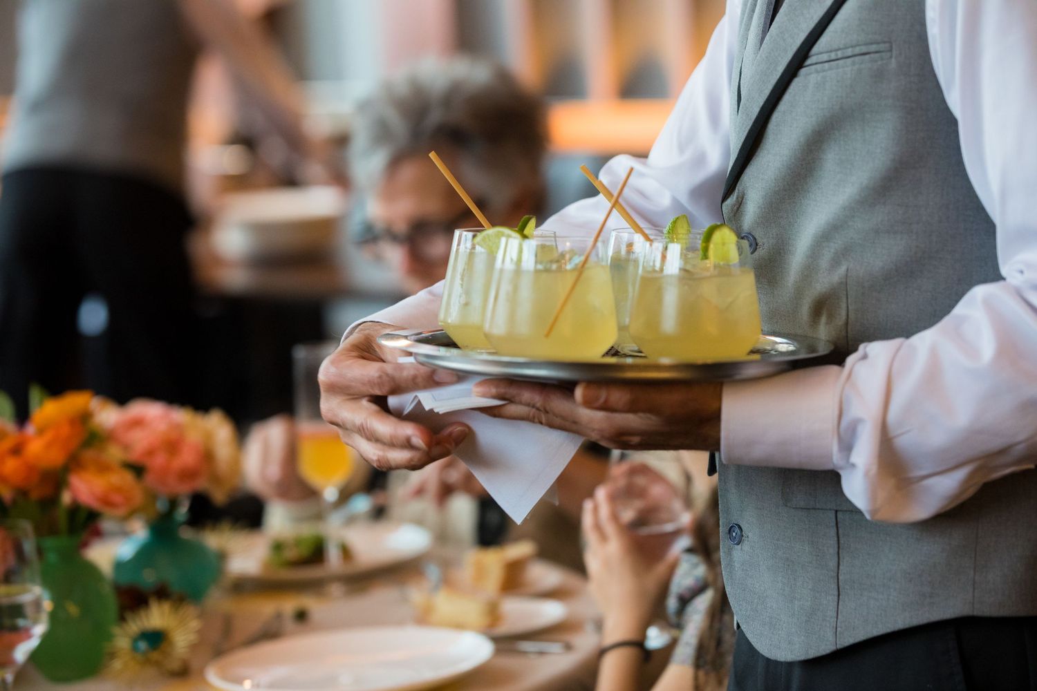 Server carrying tray of yellow cocktails at an upscale catered event.