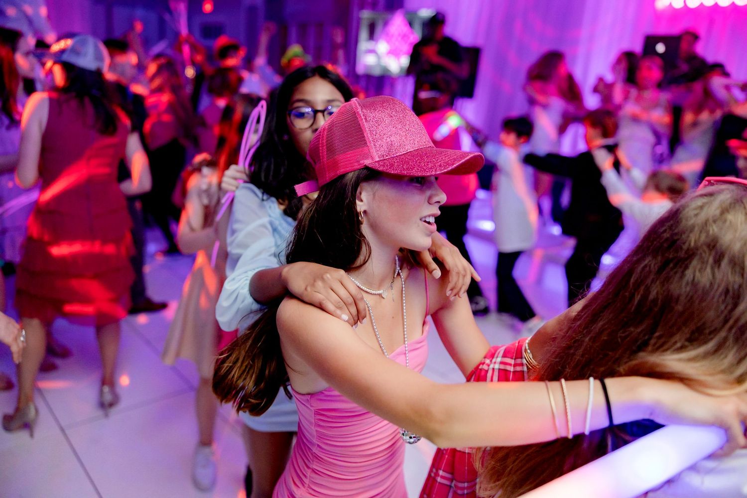 Energetic crowd dancing and celebrating at a pink-lit party venue.