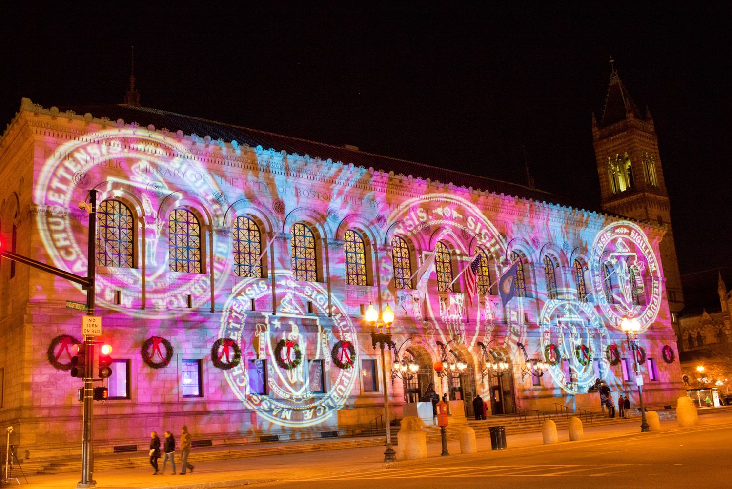 Historic building facade illuminated with vibrant pink and purple lights and projected geometric patterns.