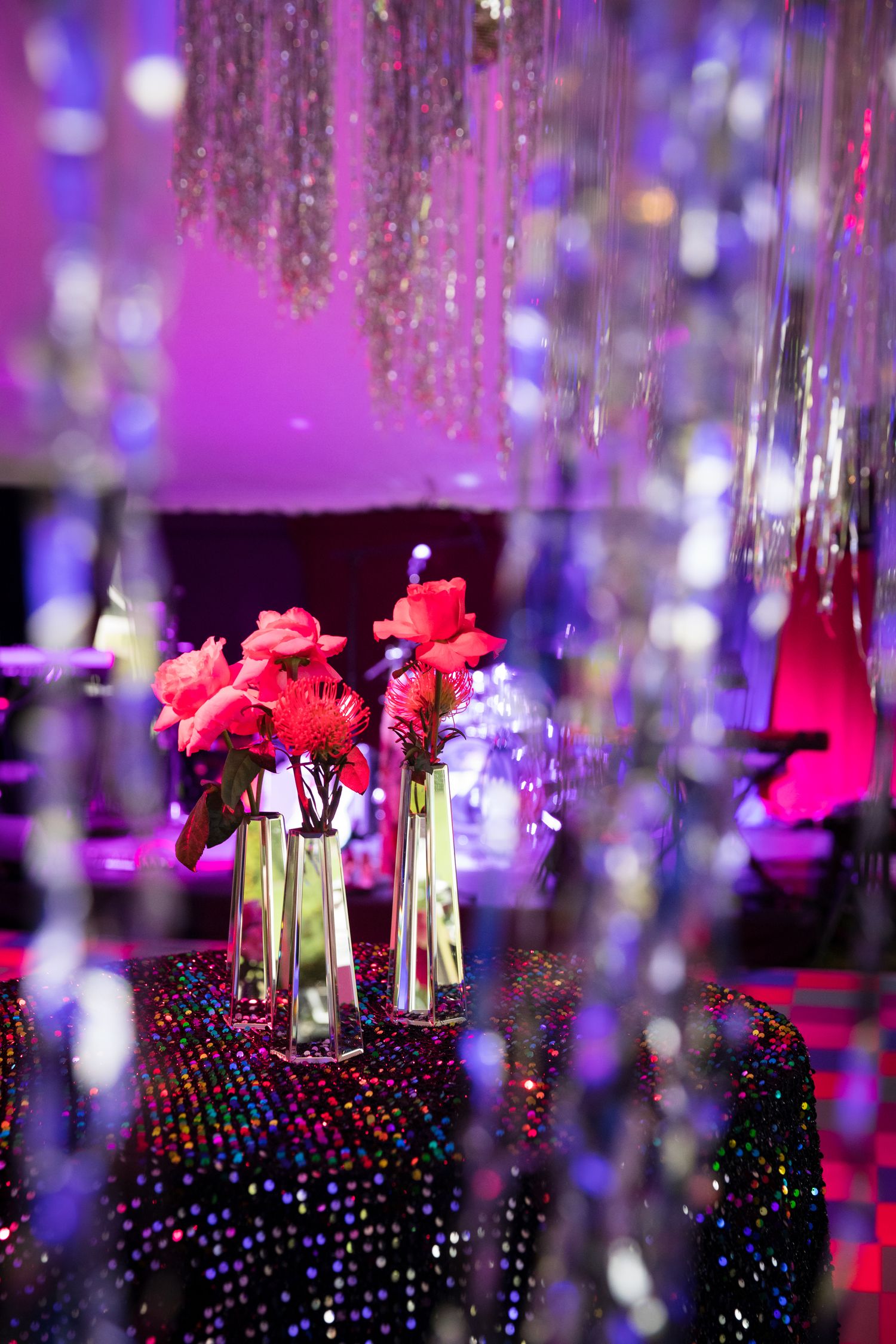 Pink roses in glass vases with crystal decorations and purple lighting create an elegant party atmosphere.