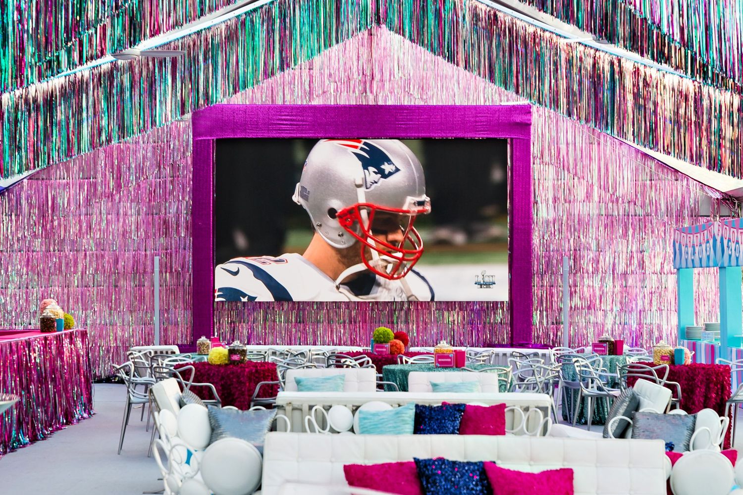 A sports-themed party room decorated with pink metallic streamers and a large display screen showing a football game.