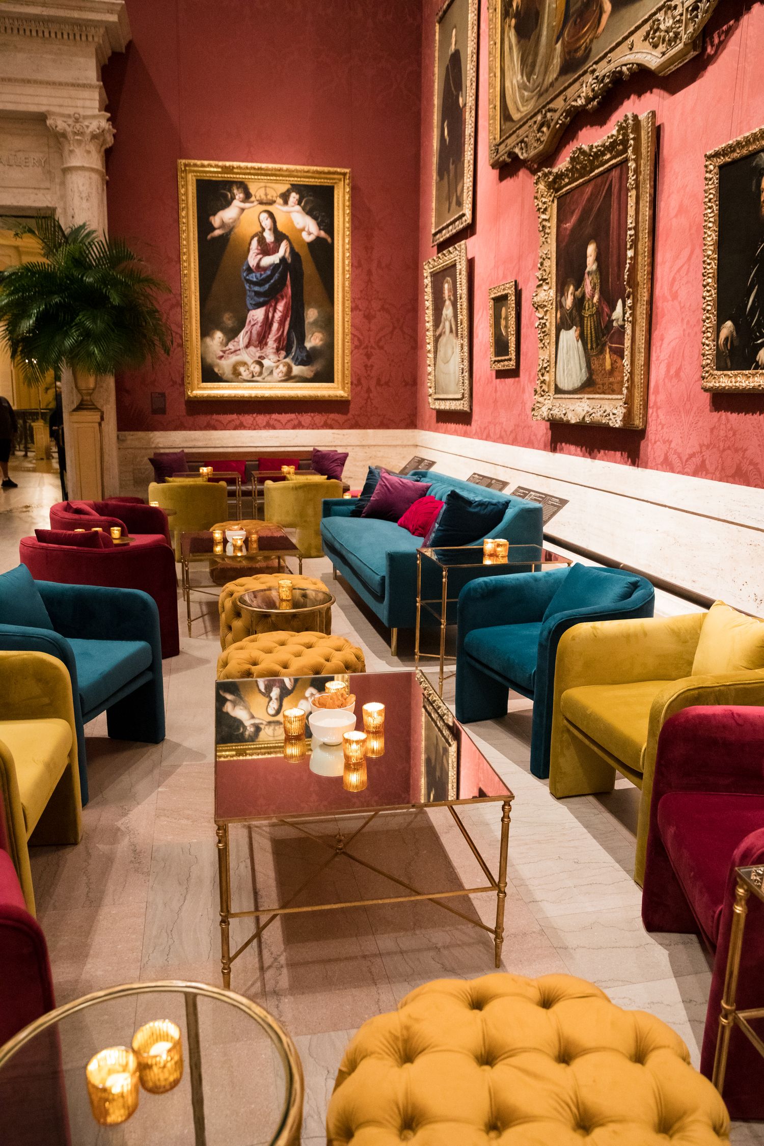 Luxurious lounge area with colorful velvet furniture and classical artwork in ornate gold frames.