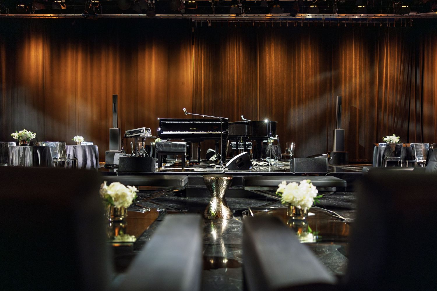 Grand piano on stage with elegant table settings and floral arrangements in dramatic lighting.