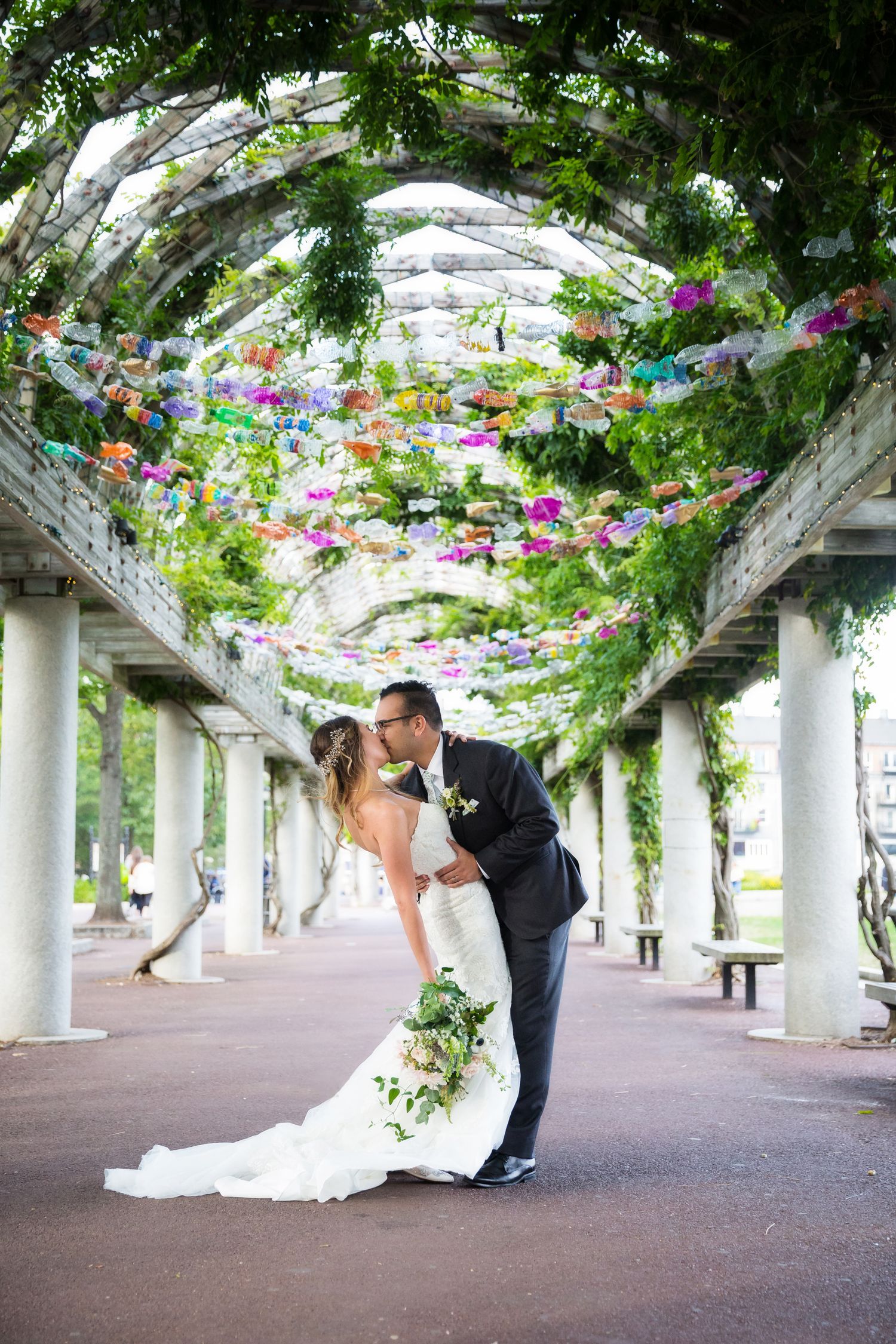 A romantic moment under a floral archway with white columns and pink flowers creating an enchanting garden walkway.