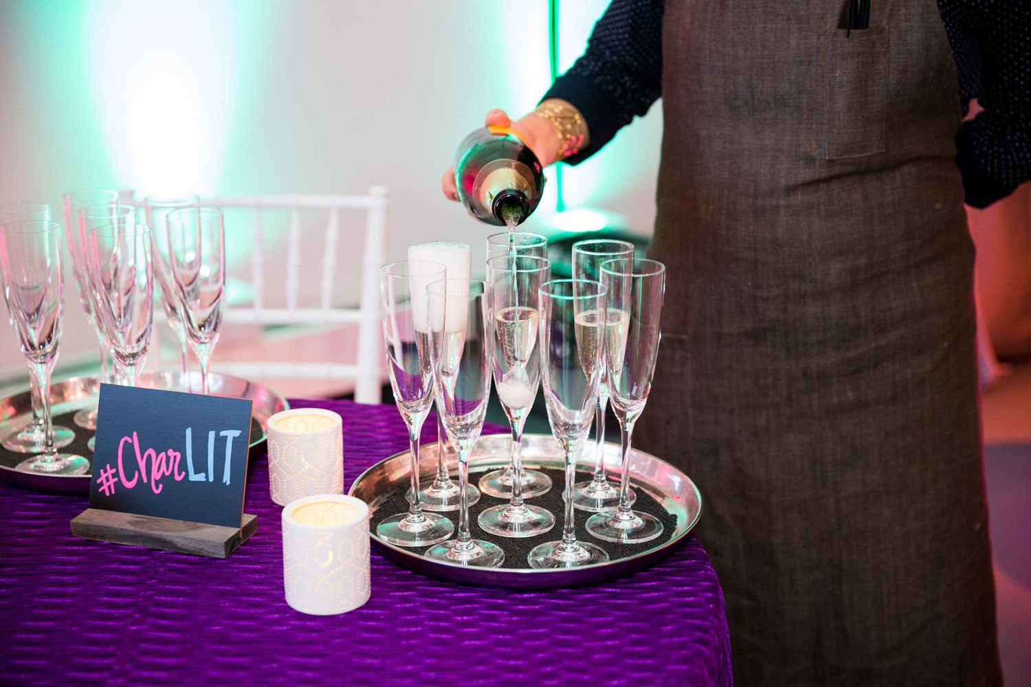 Server pouring champagne into flutes on a purple-clothed table at an event.