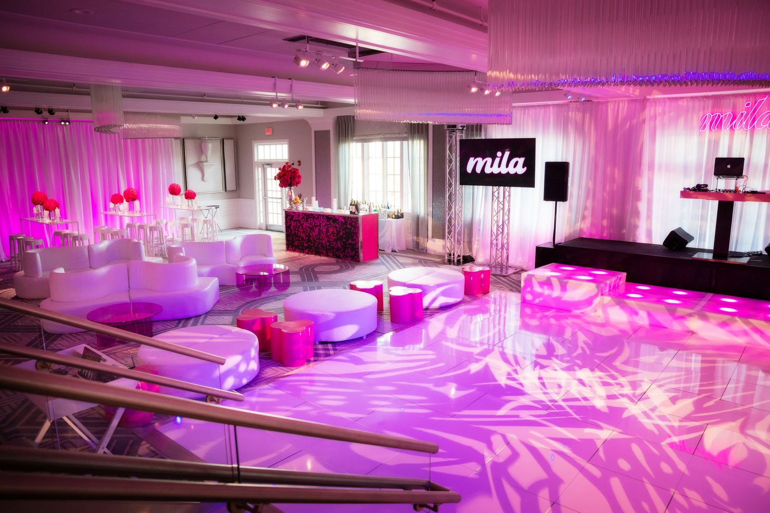 Event space decorated with pink uplighting, white furniture and projected patterns on the floor.