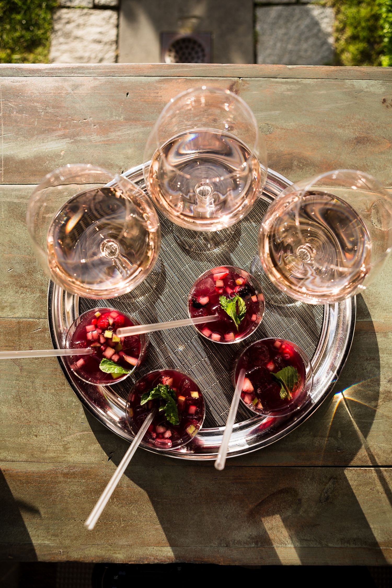 Rose wine glasses and fresh cherries arranged on a silver serving tray in sunlight.