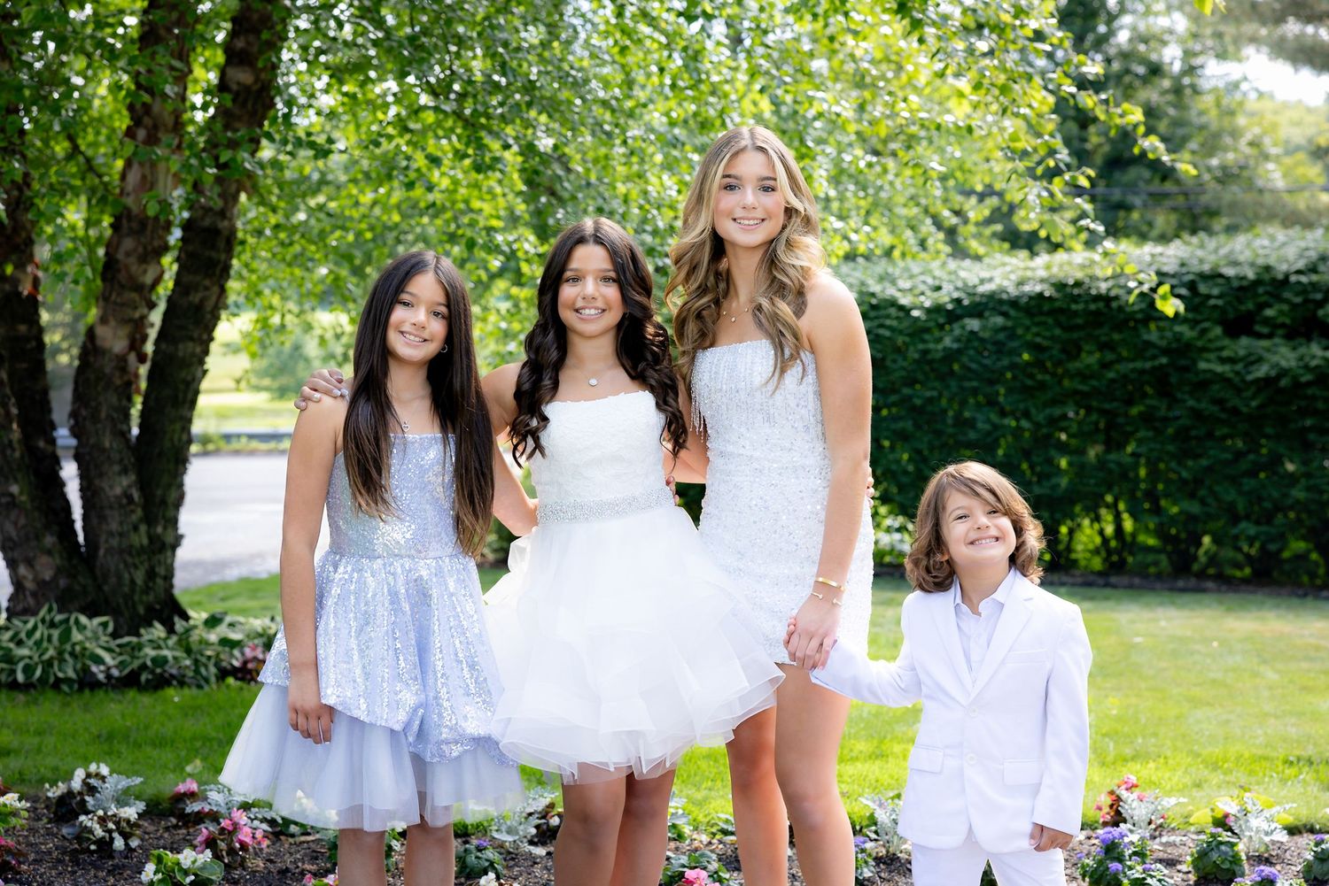 A group stands together on a garden path wearing coordinated white and light blue dresses.