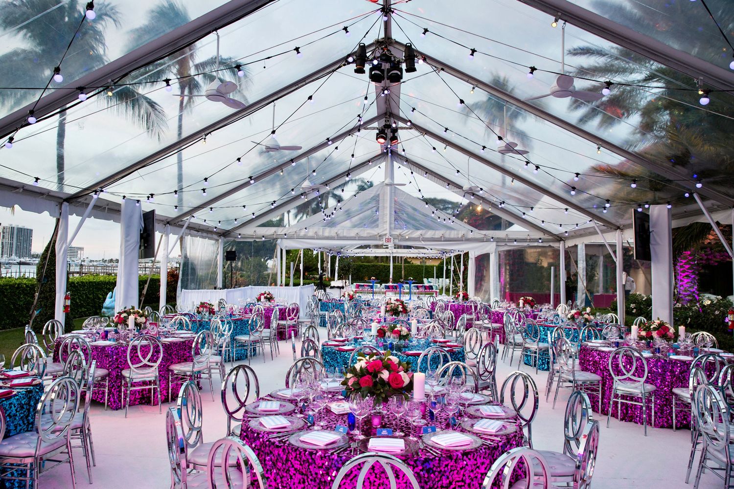 Clear tent reception space with purple decor, string lights, and elegant table settings.