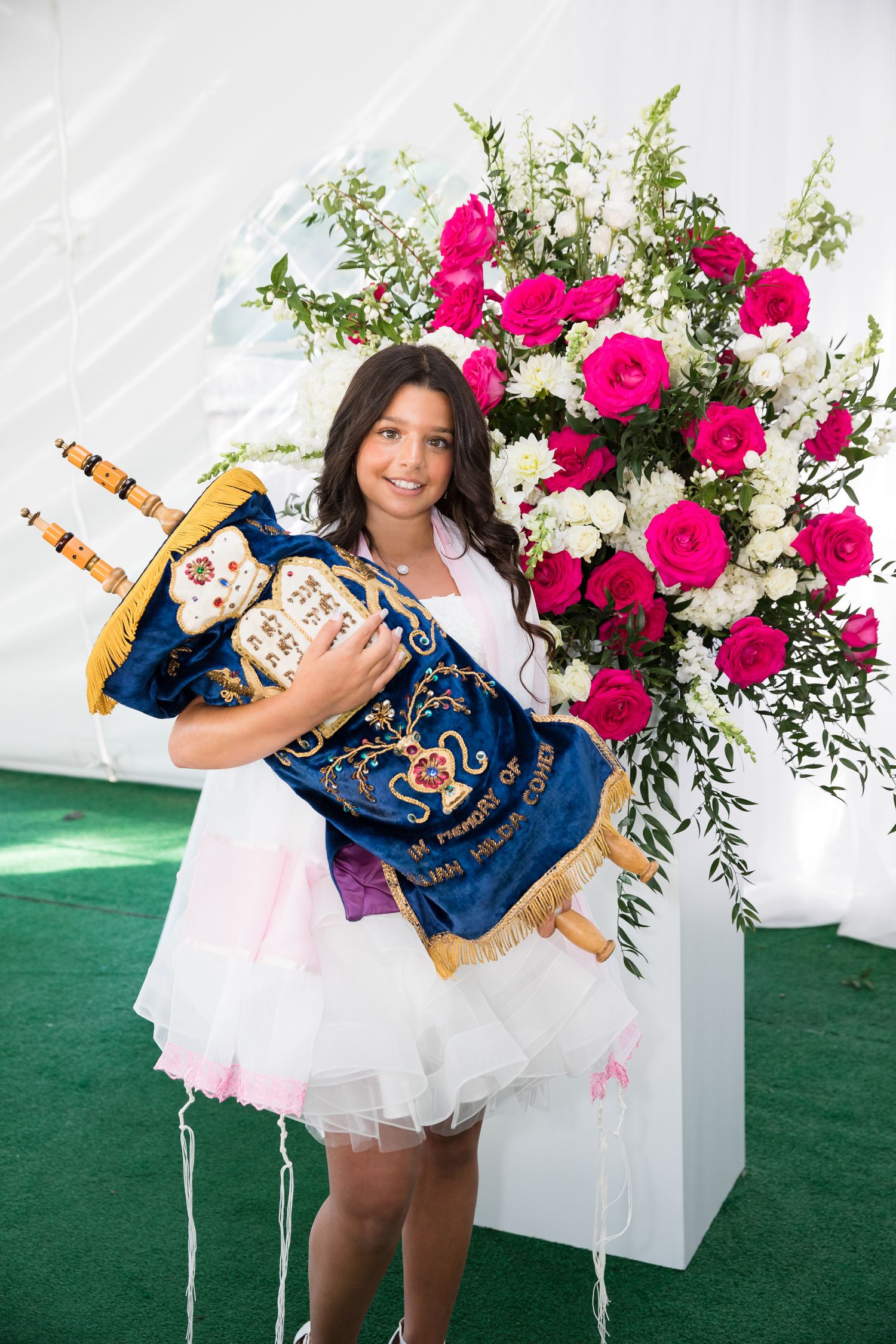 A traditional ceremony participant holds decorative items next to vibrant pink and white floral arrangement.