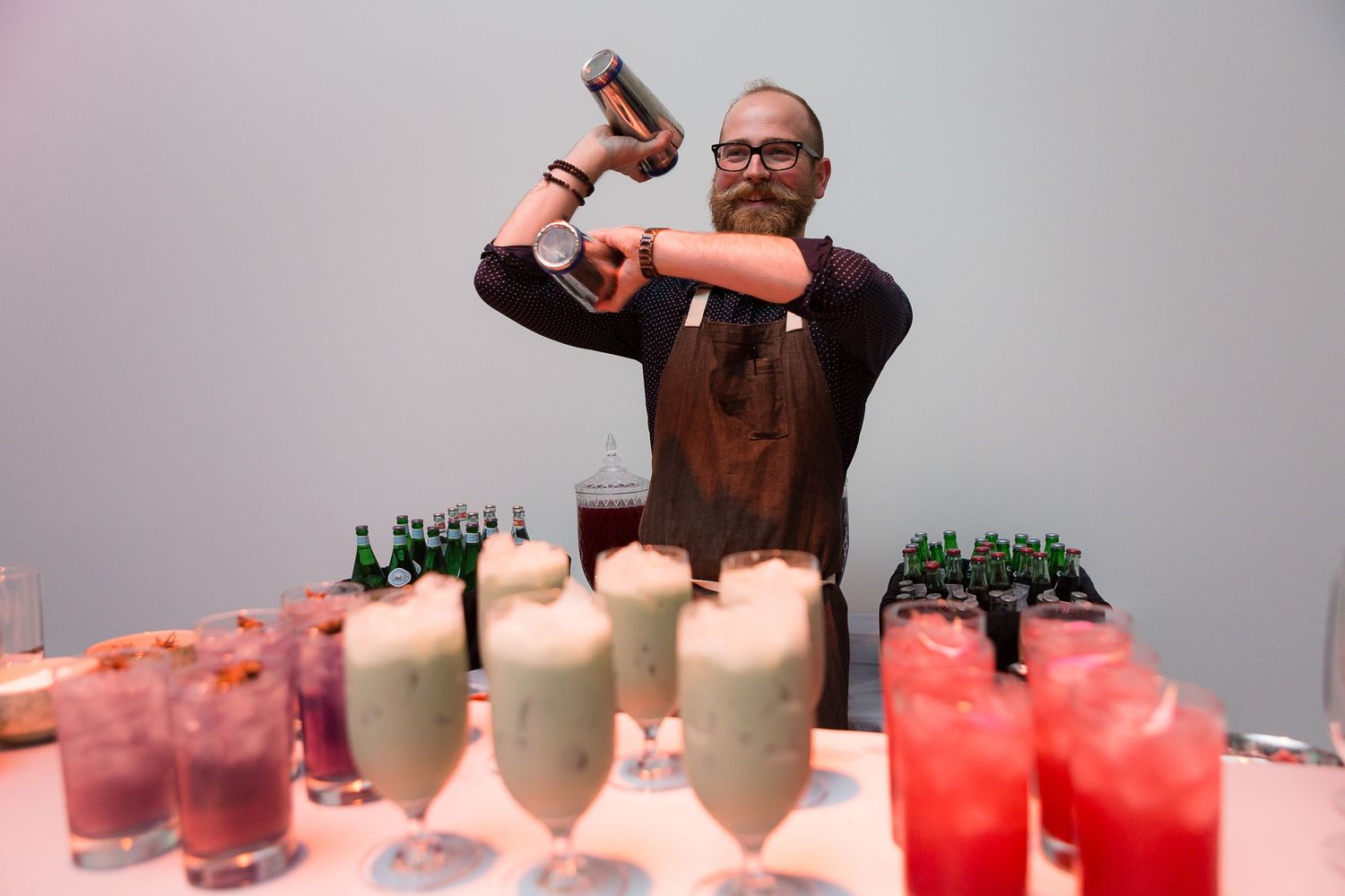 Bartender pouring cocktails at an event with multiple colorful drinks on display.