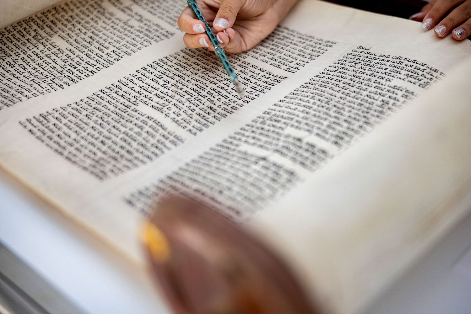 A close-up view of hands pointing to text in an ancient religious manuscript.