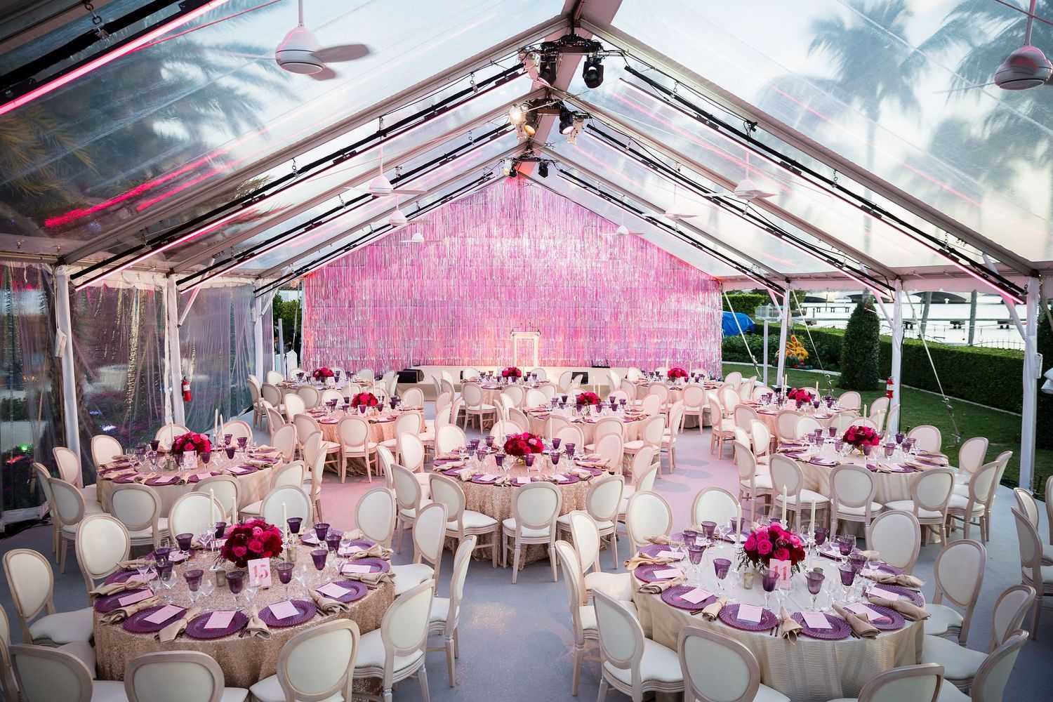 Elegant pink and white wedding reception setup under a clear tent with hanging decor.
