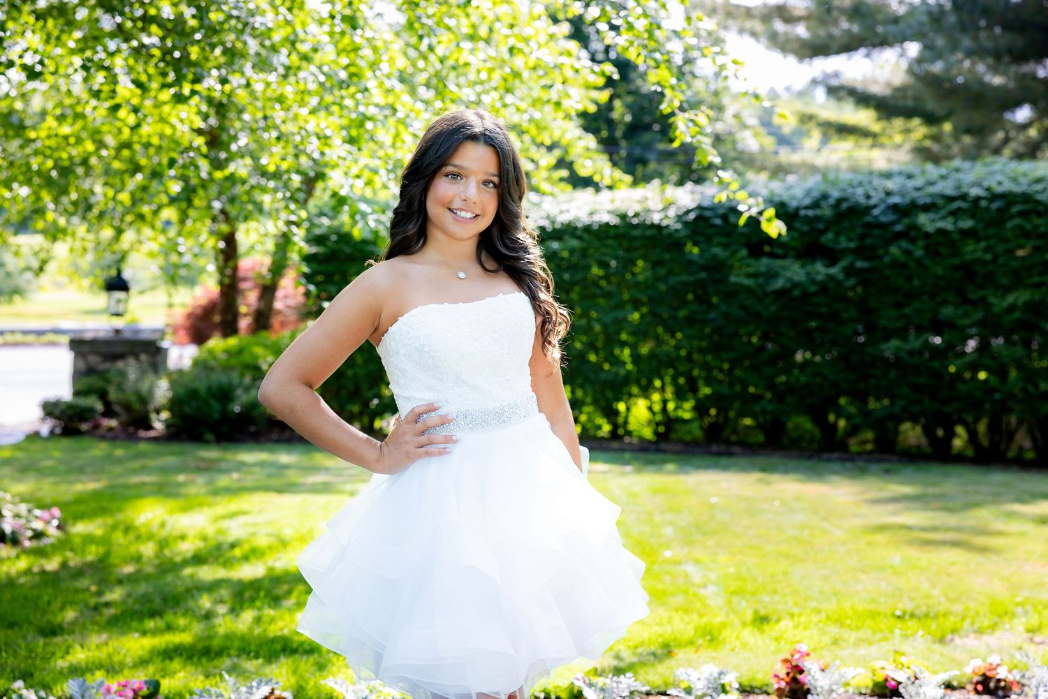 A white strapless tulle dress is worn outdoors in a sunny garden setting.