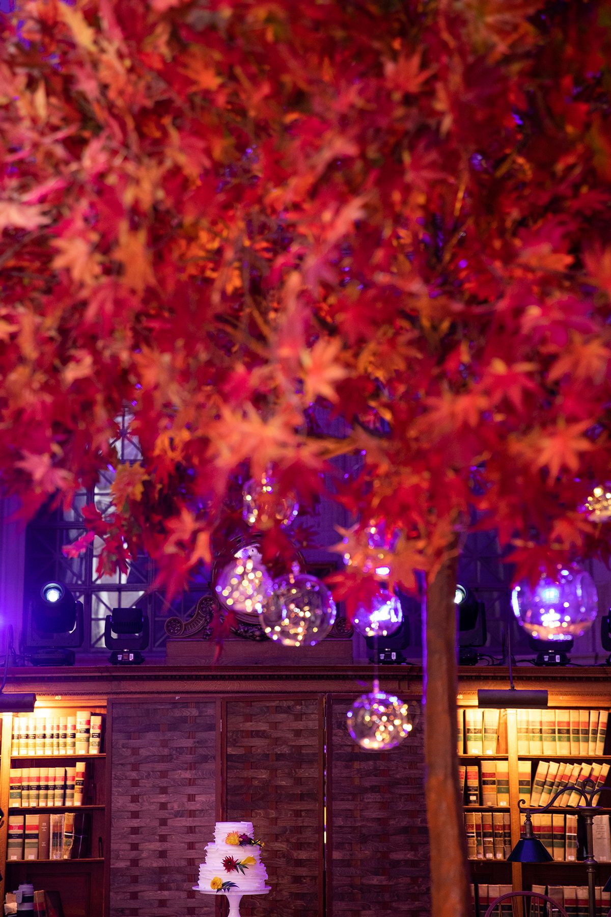 Vibrant red maple leaves illuminated by purple lighting with hanging glass orb decorations.