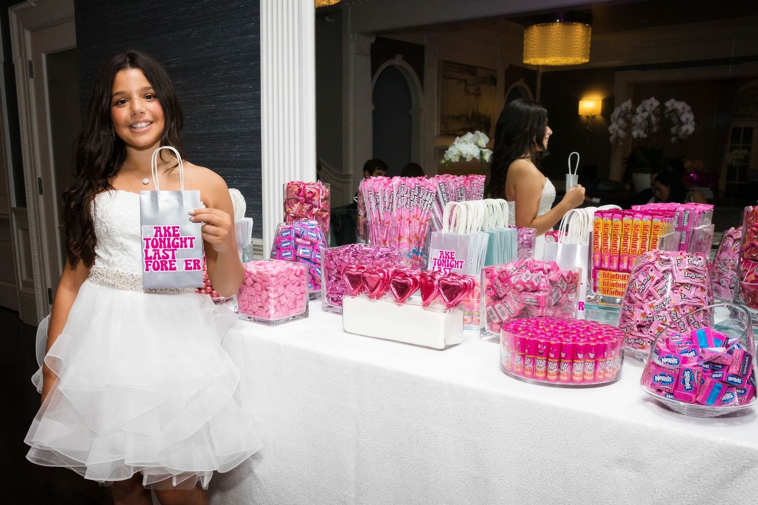 White-dressed attendant standing behind table with pink party favors and decorations.