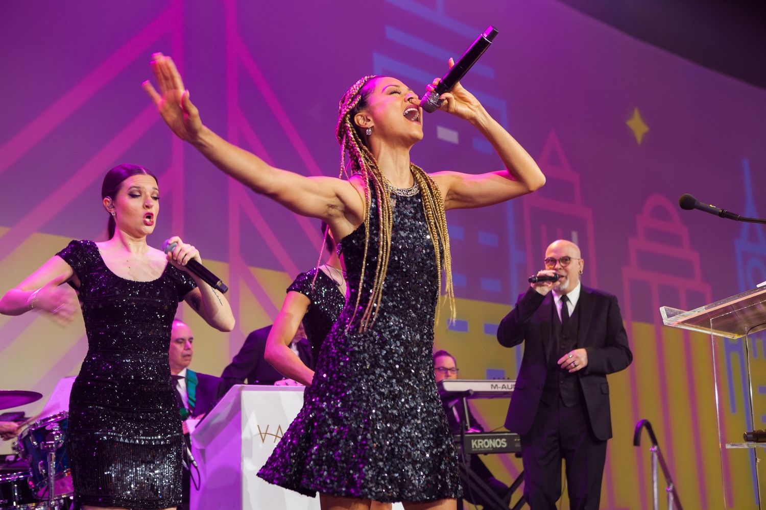 Performers on stage during an energetic musical performance with purple lighting effects.