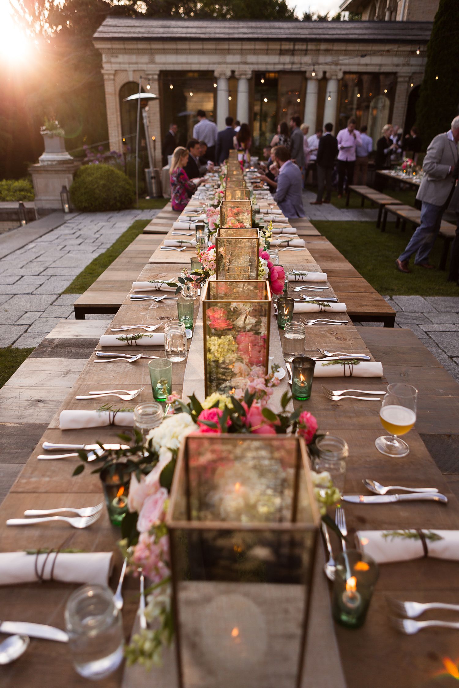 Long outdoor dining table set with elegant decor and floral centerpieces at sunset.