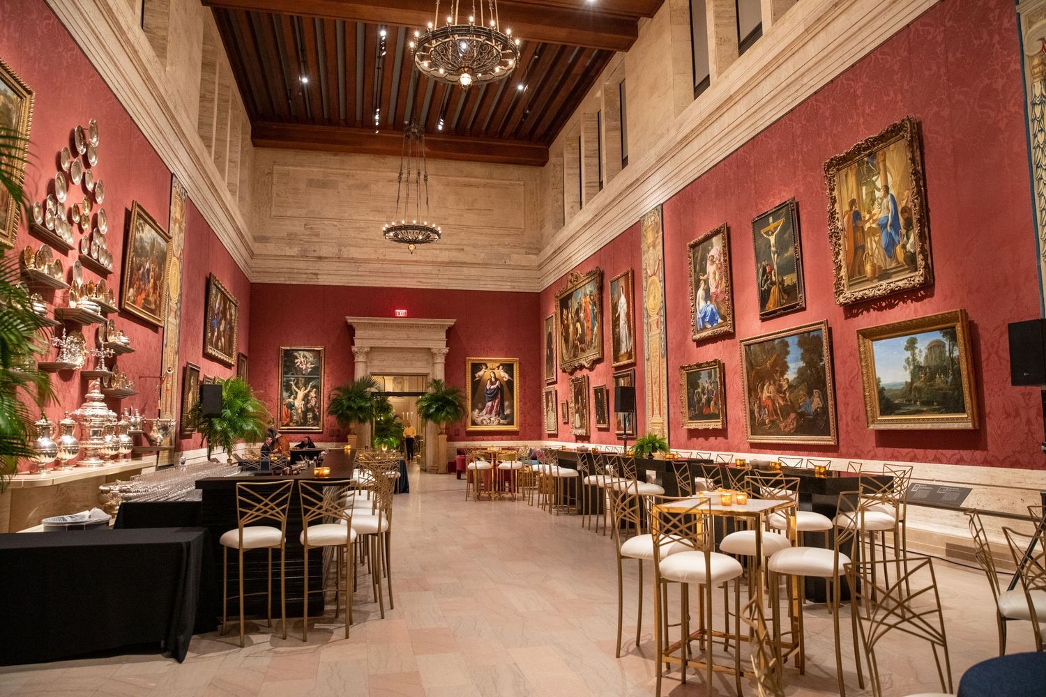 Elegant dining hall with red walls adorned with classical paintings and high wooden beam ceiling.