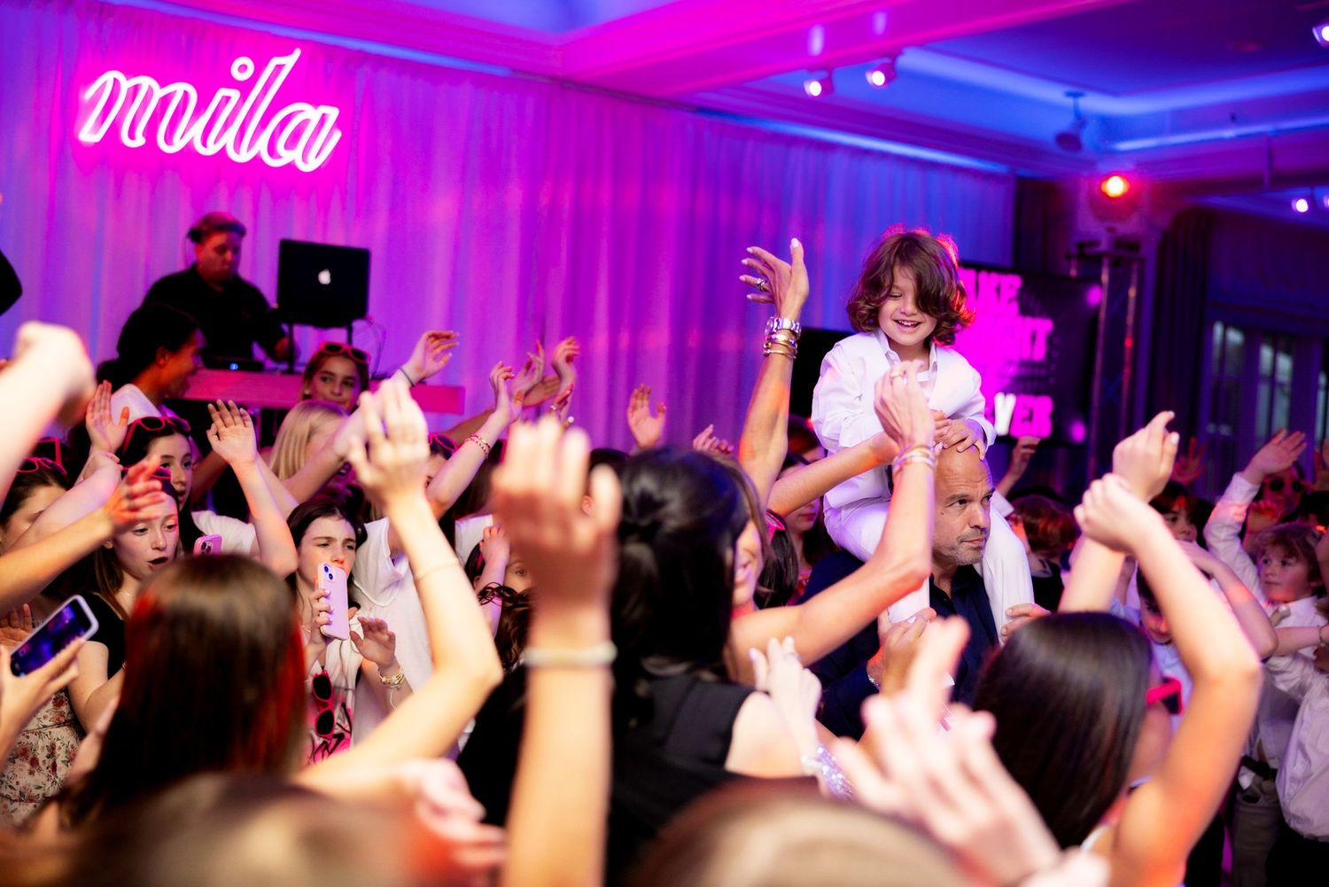 Crowd dancing with raised hands at a nightclub event under neon lighting.