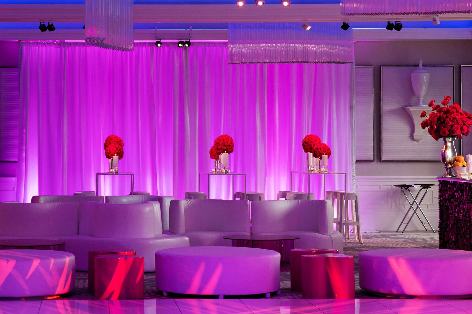 Elegant event space with purple lighting, white seating, and red floral arrangements.
