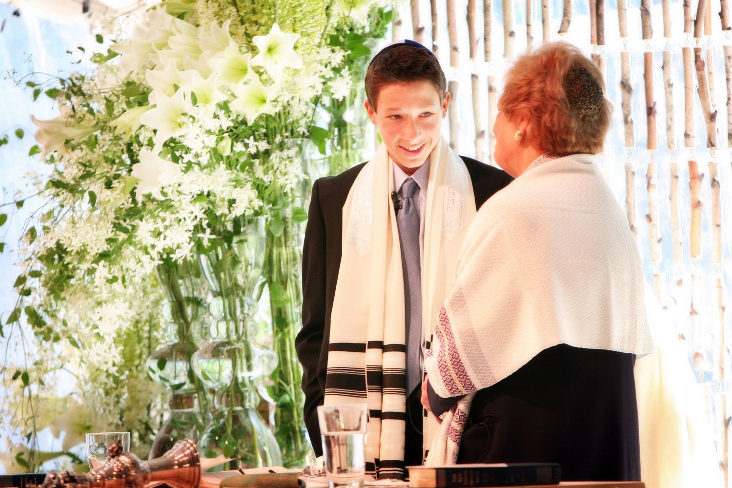 Religious ceremony taking place with floral decorations and white backdrop.
