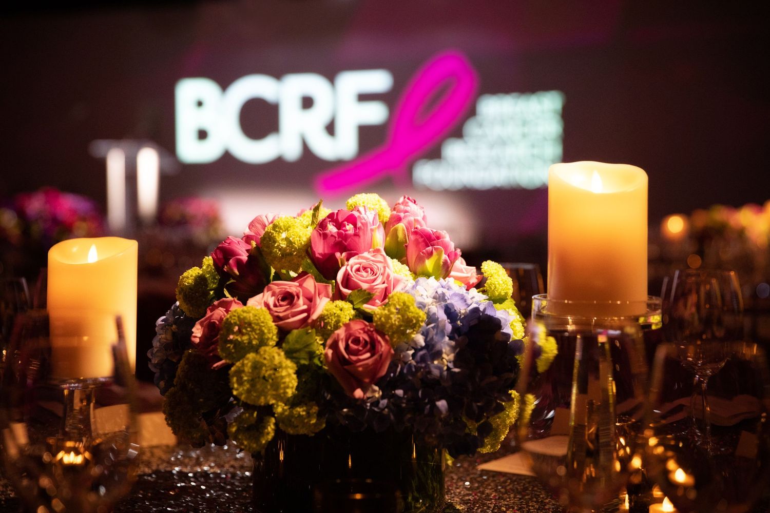 Elegant table setting with floral centerpiece and candles under BCRF event signage.