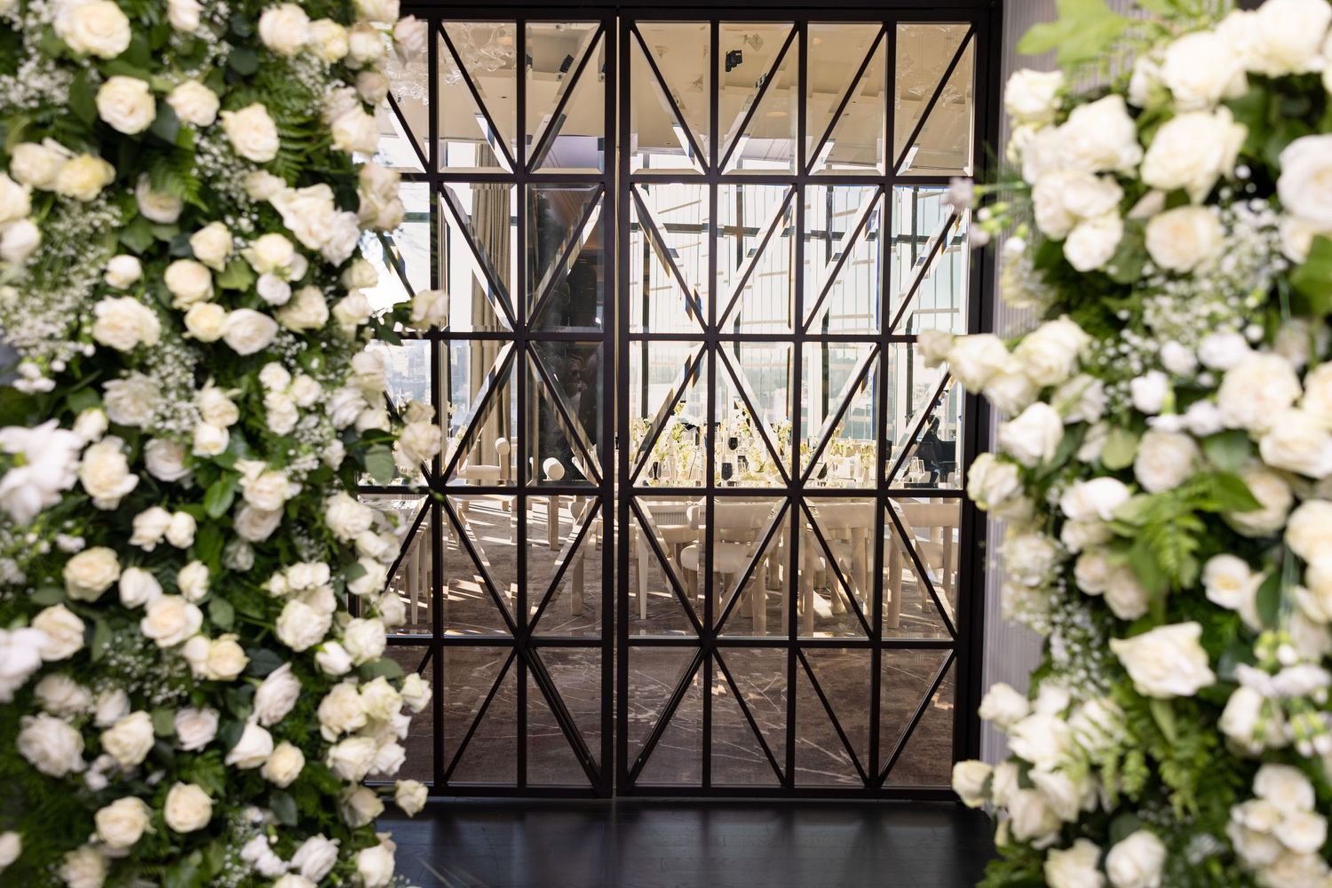 Geometric iron window frame surrounded by blooming white roses and greenery.